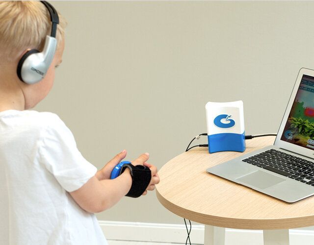 En person med hodetelefoner og en håndleddsmontert sensor samhandler med en bærbar PC og en sensor på et trebord.