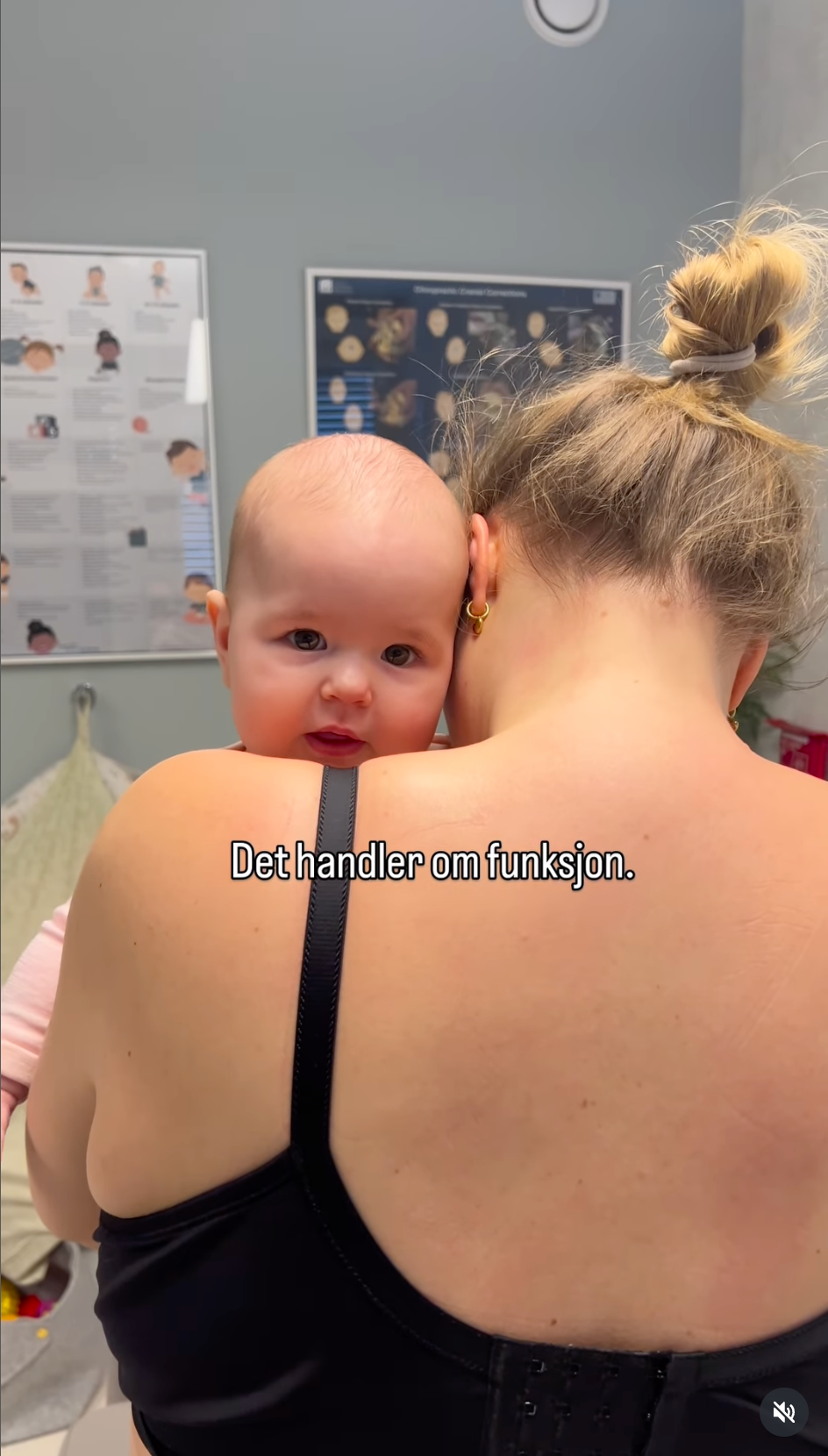 En person holder en baby mot skulderen sin i et rom med medisinske plakater på veggen.