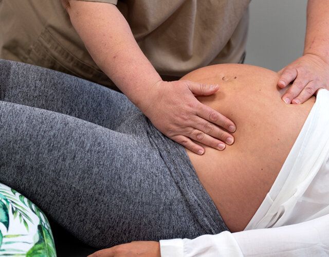 En person palperer magen til en gravid person som ligger på siden.