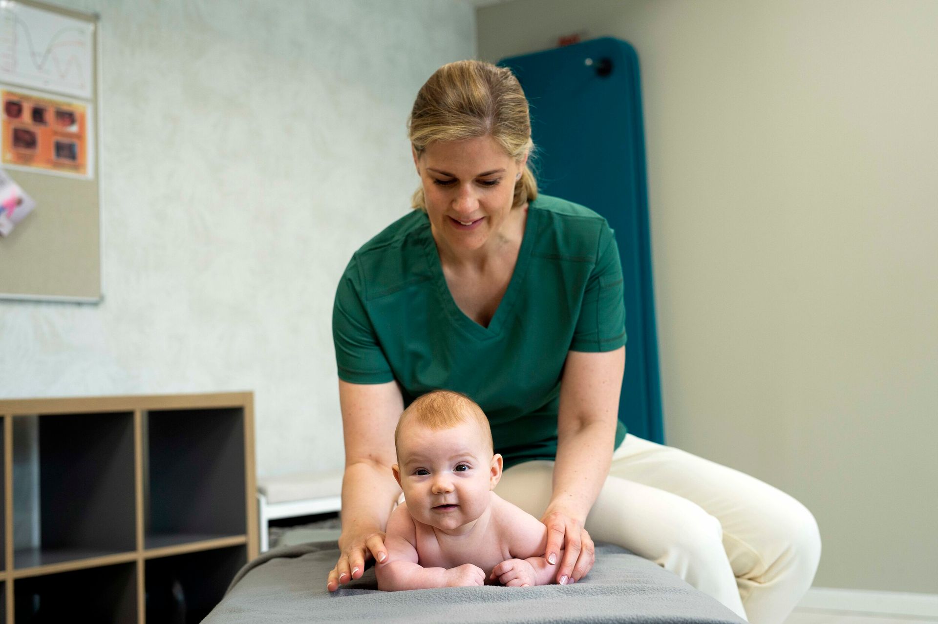 En person i en grønn skjorte hjelper en baby med å øve på magetid på et polstret bord i en klinisk eller terapisetting.