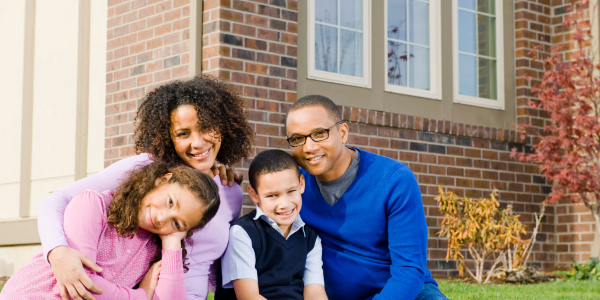 family sitting in front of house with homeowners insurance