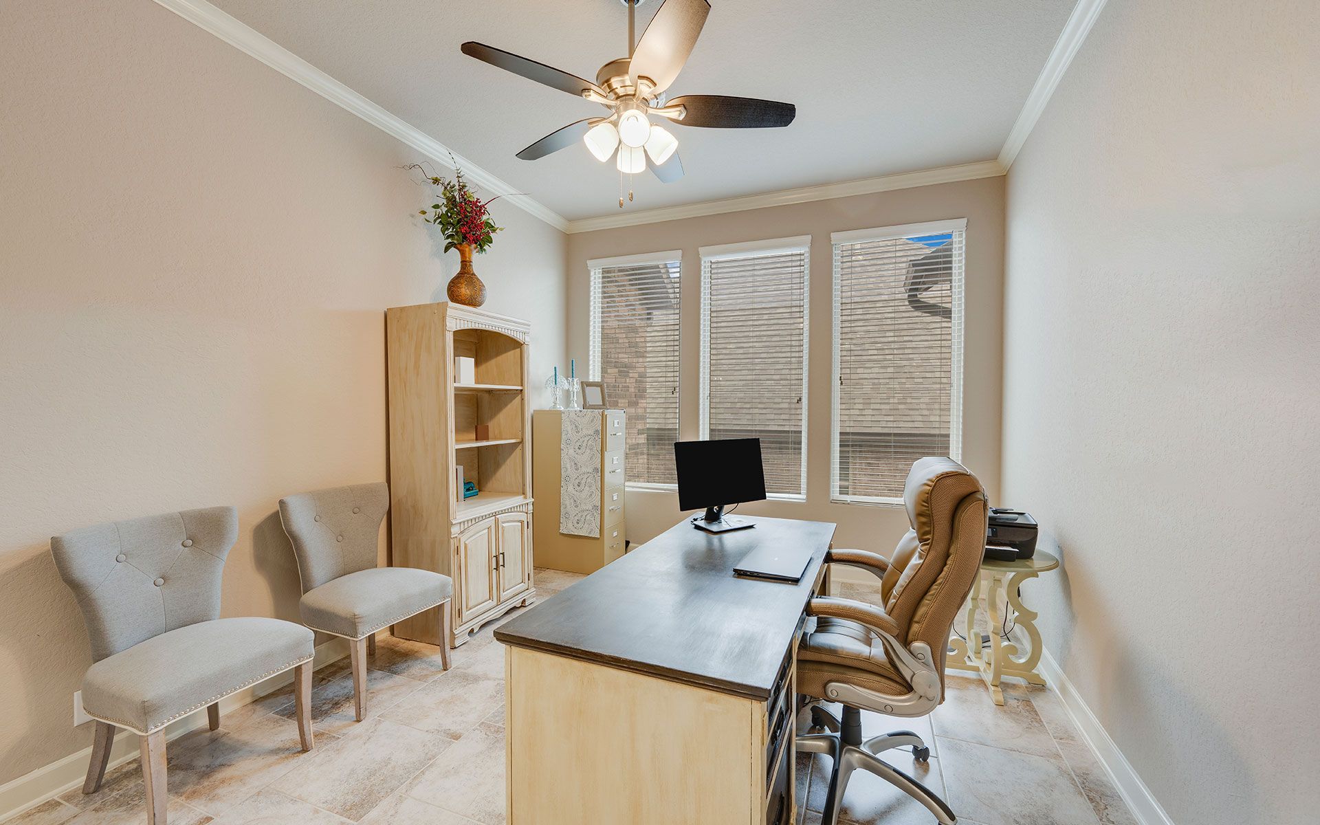 A home office with a desk , chairs , and a ceiling fan.