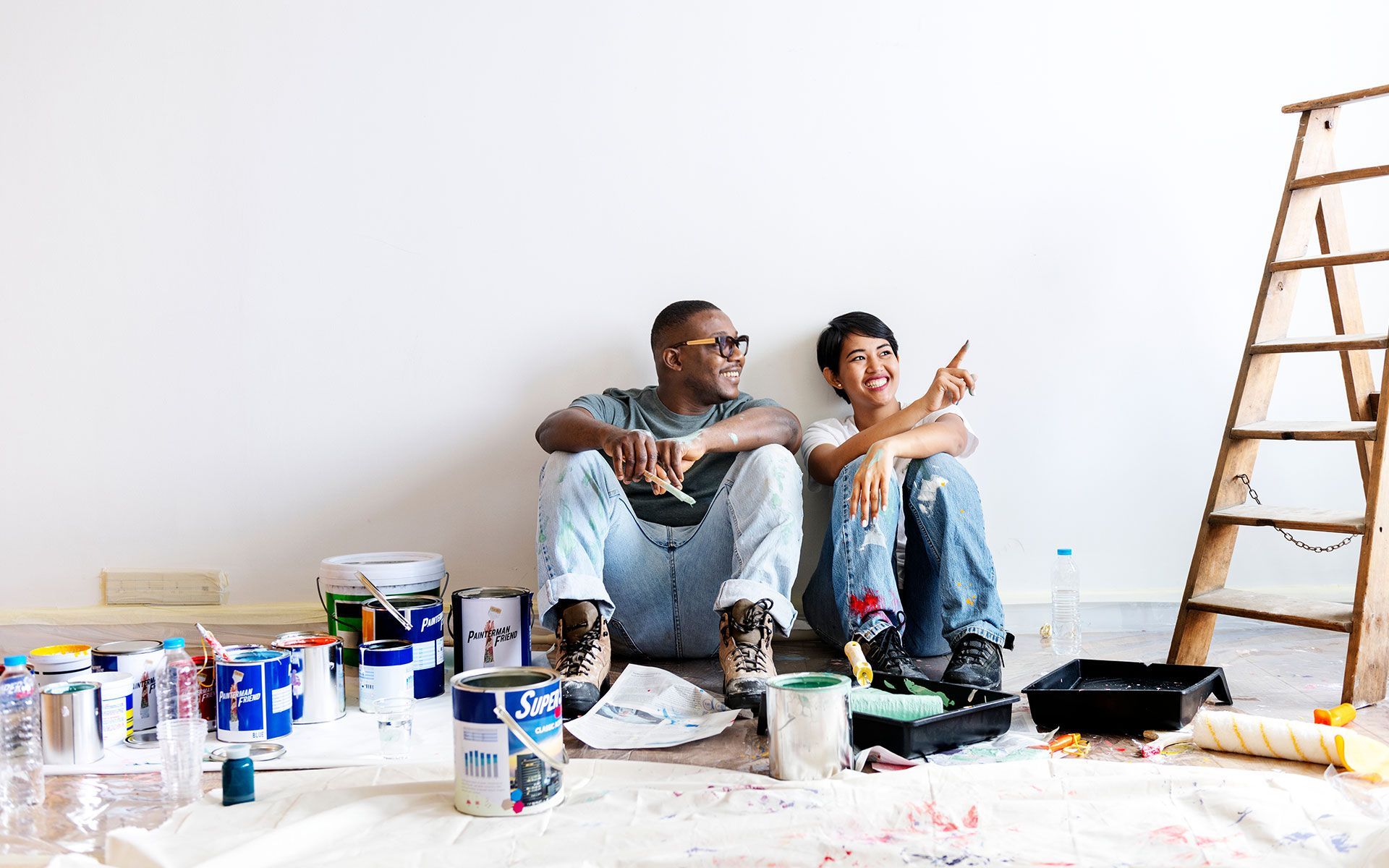 A man and a woman are standing in an empty room looking at a blueprint.