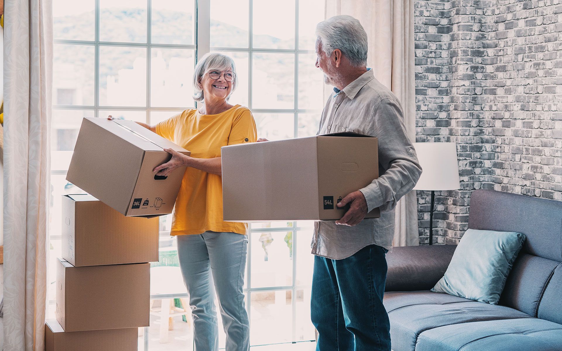 A man and a woman are holding cardboard boxes in a living room.