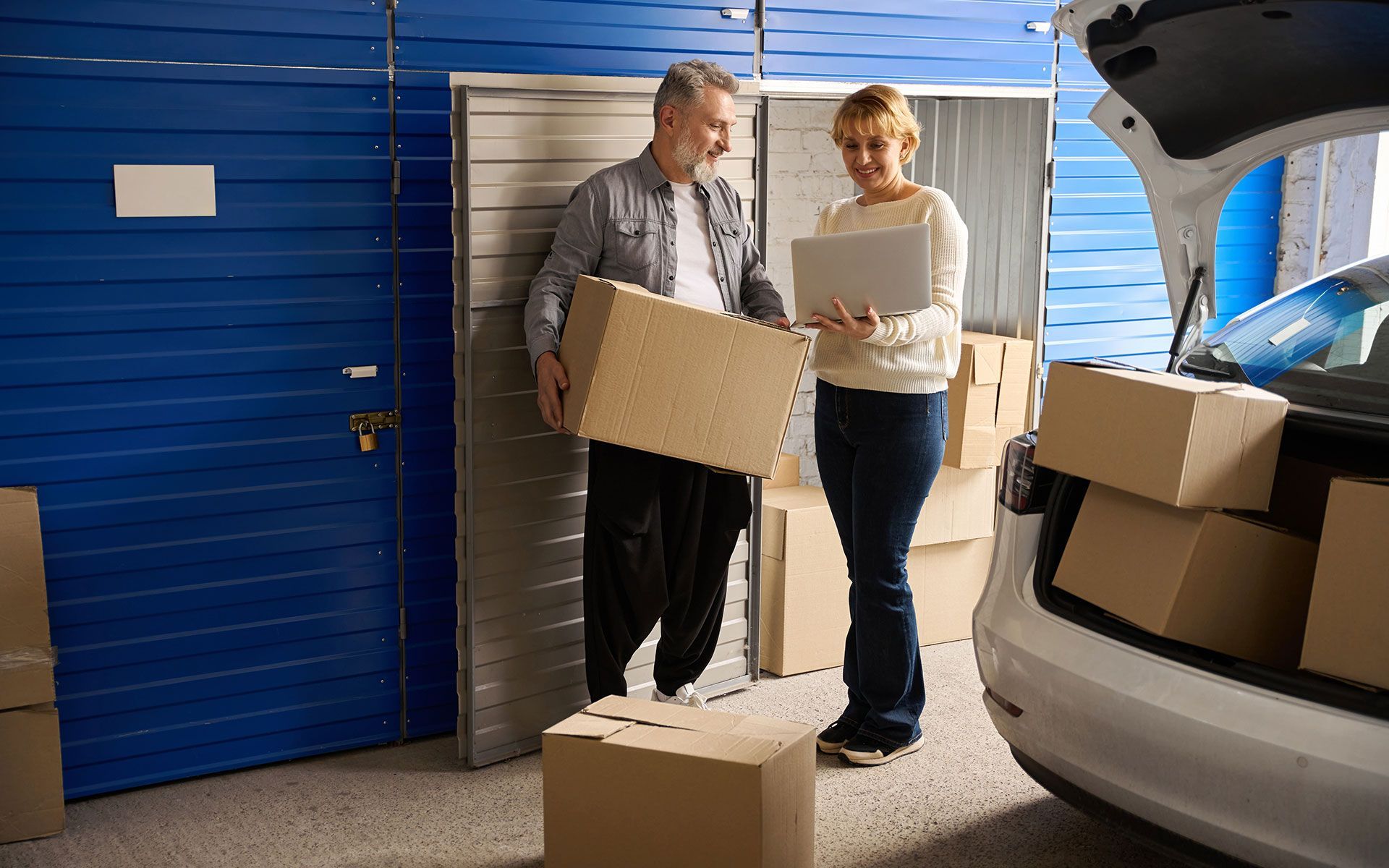 A man and a woman are loading boxes into a car in a storage unit.