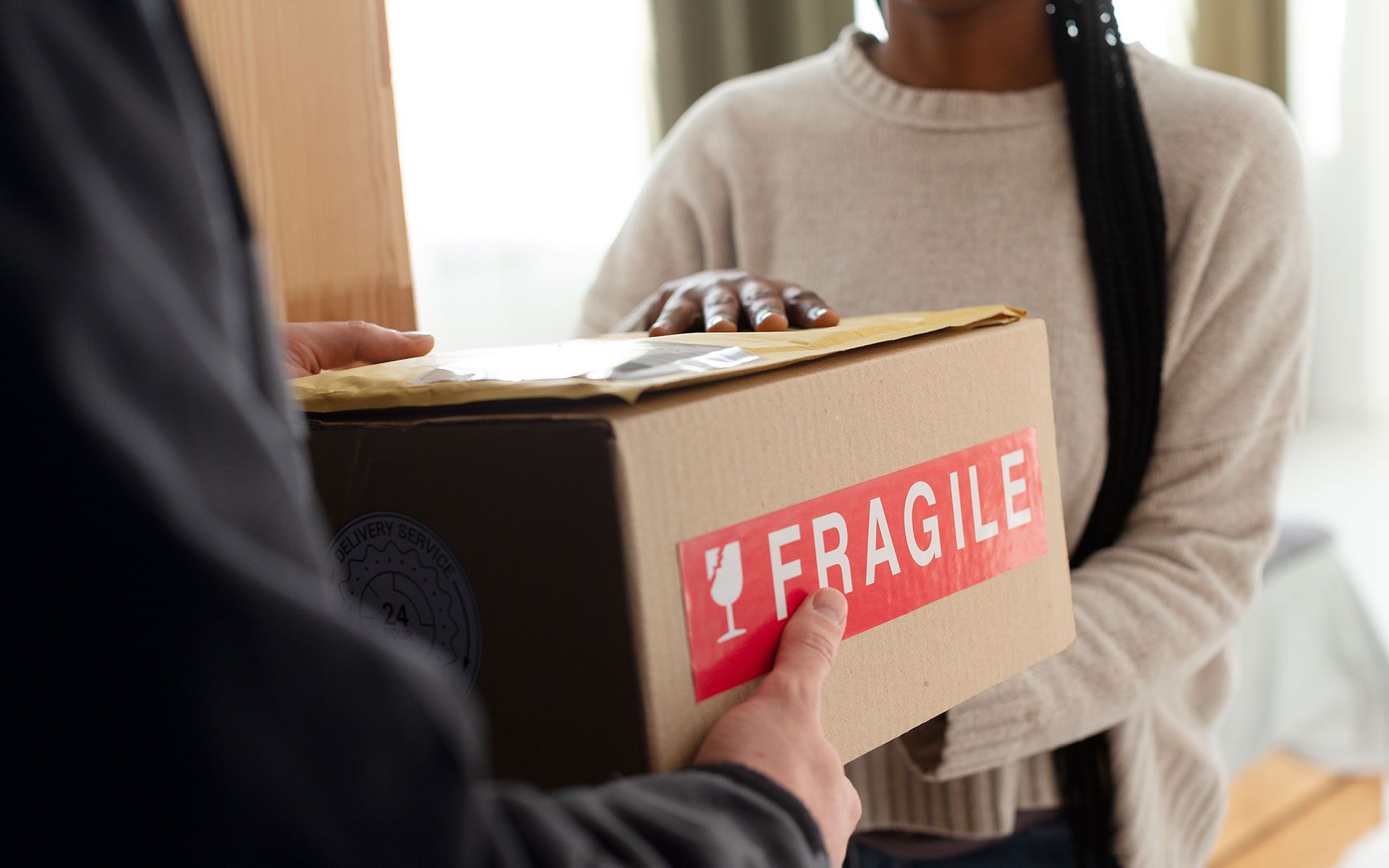 A woman is holding a cardboard box with a fragile sticker on it.