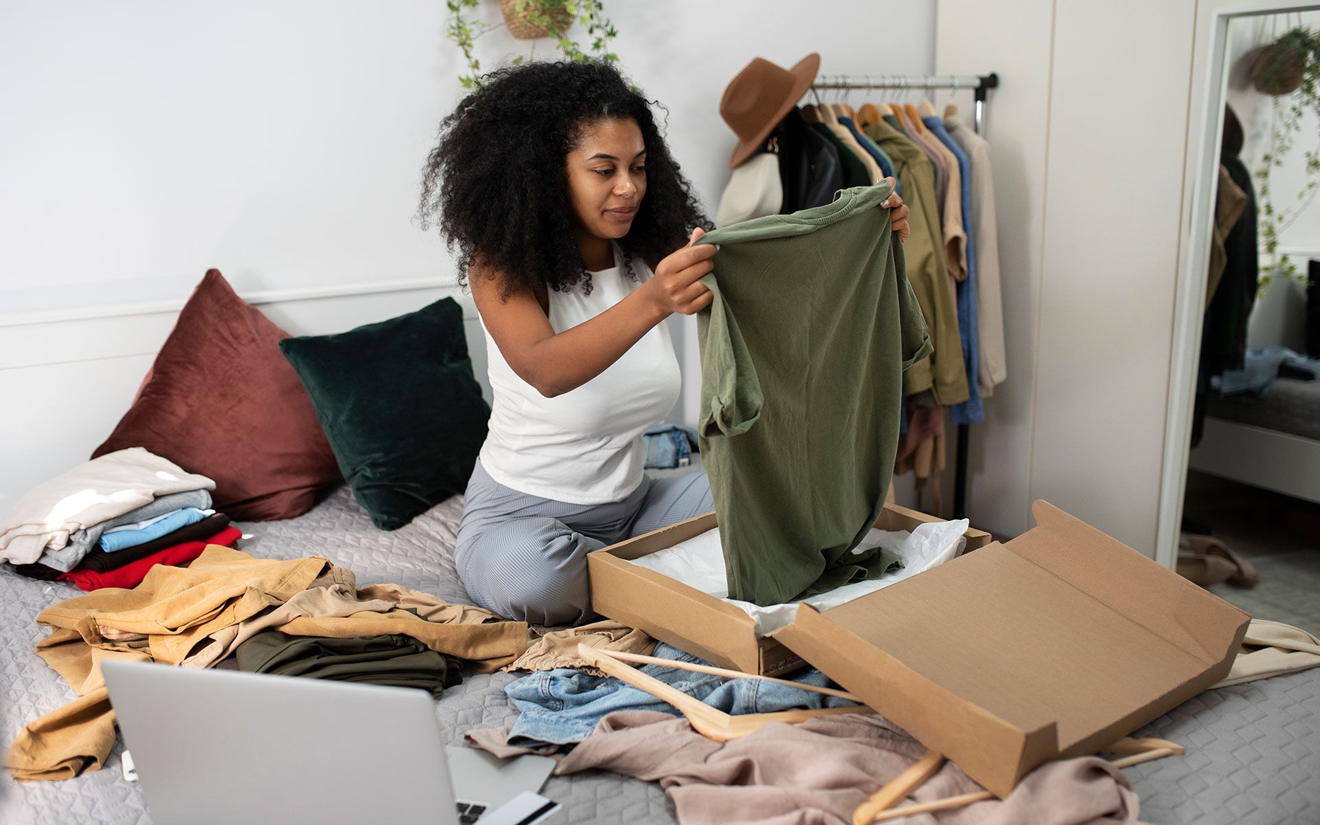 A woman is sitting on a bed looking at a box of clothes.
