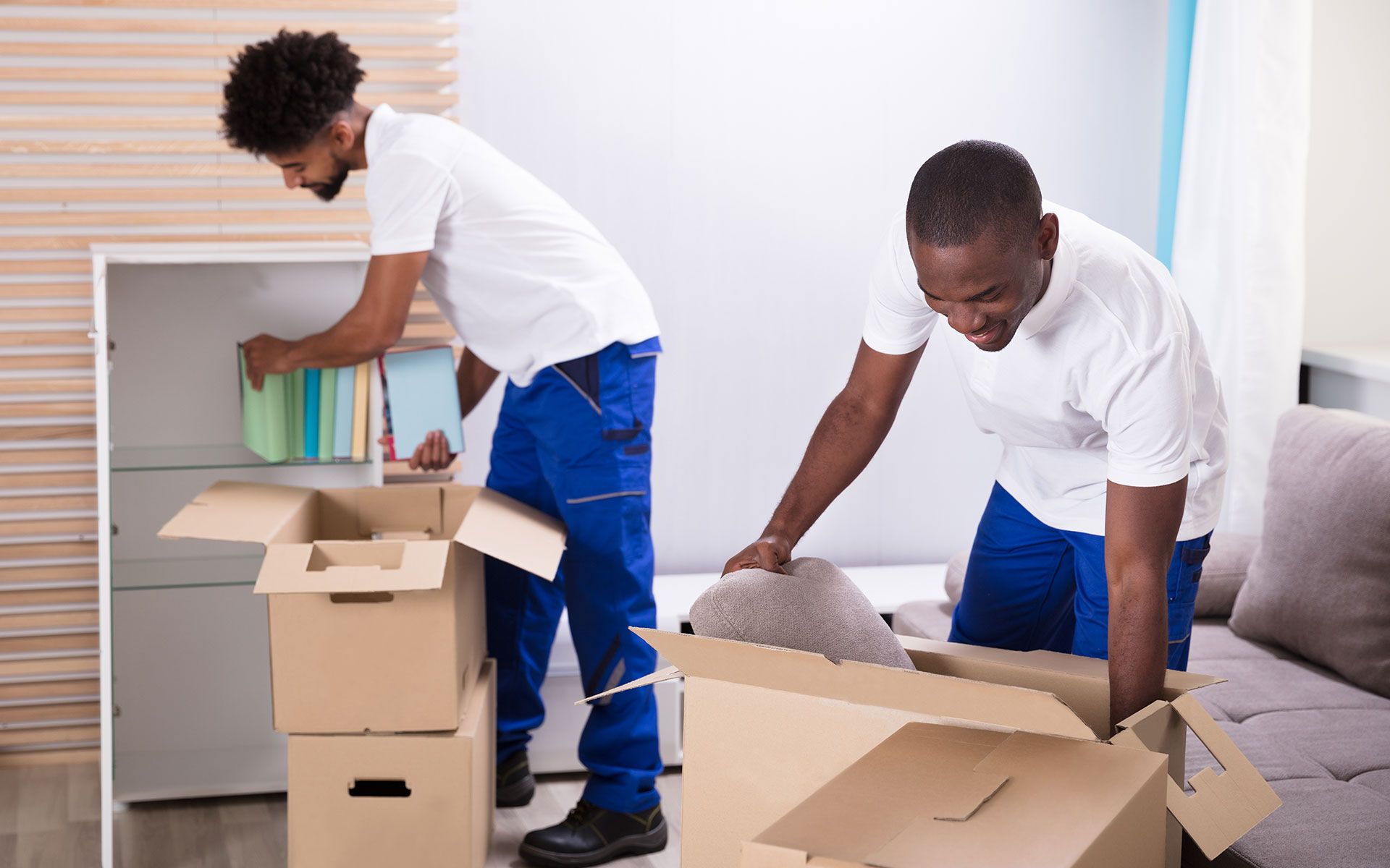 Two men are packing boxes in a living room.