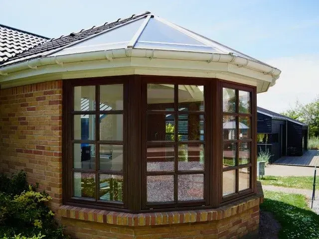 Brick sunroom with brown-framed windows and white roof on a house corner.