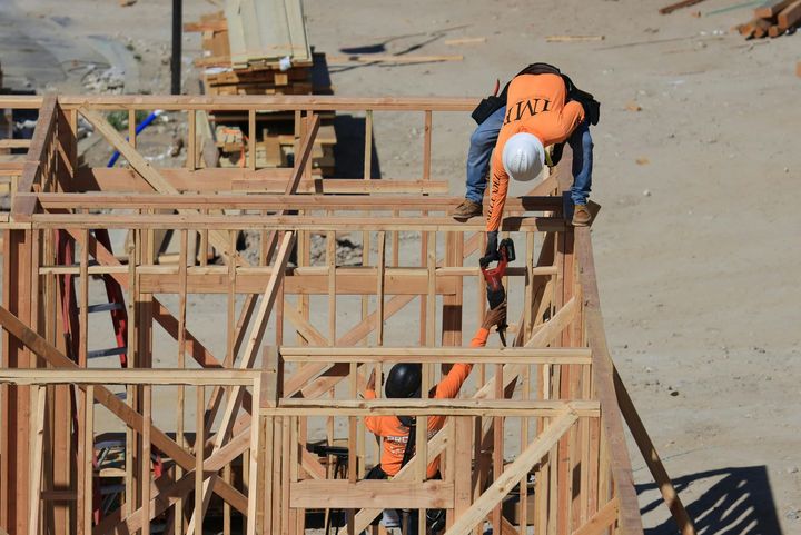 Construction workers in orange vests and hard hats on wooden framing at a building site