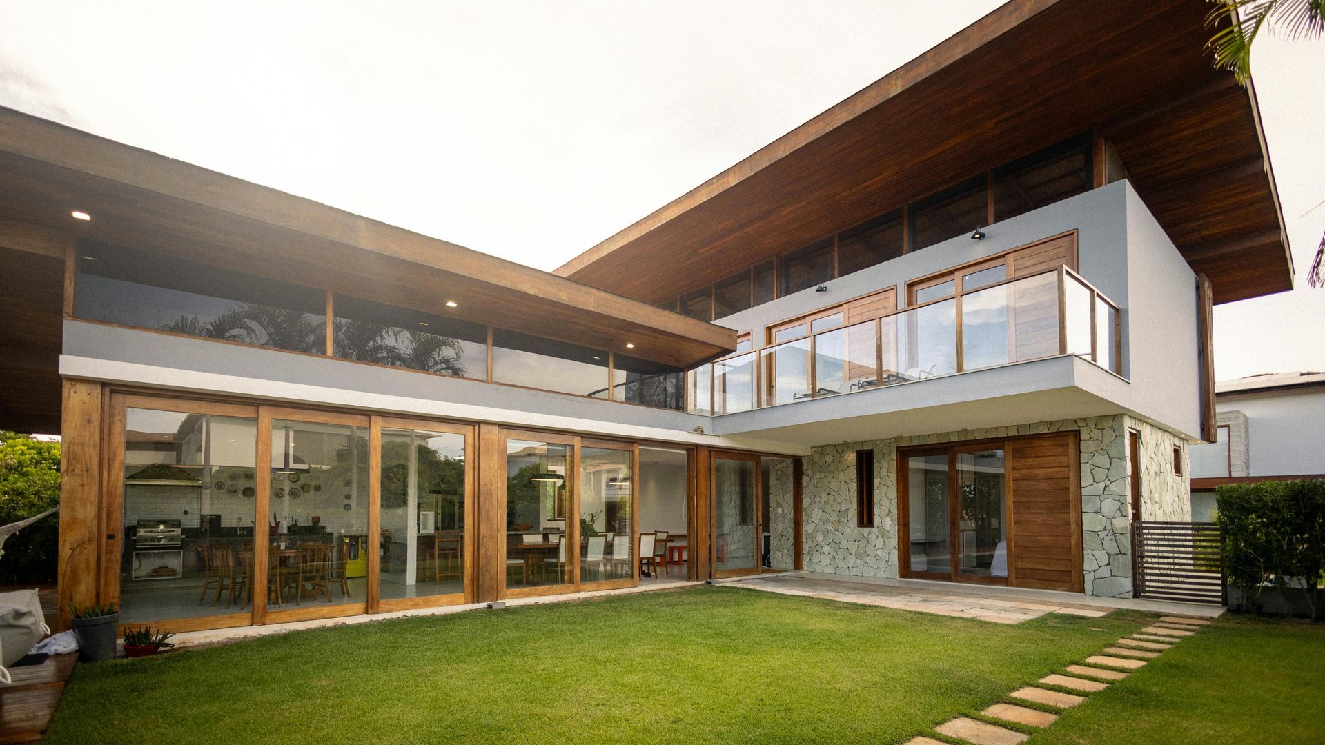 Modern two-story house with large glass doors, balcony, and green lawn in bright daylight