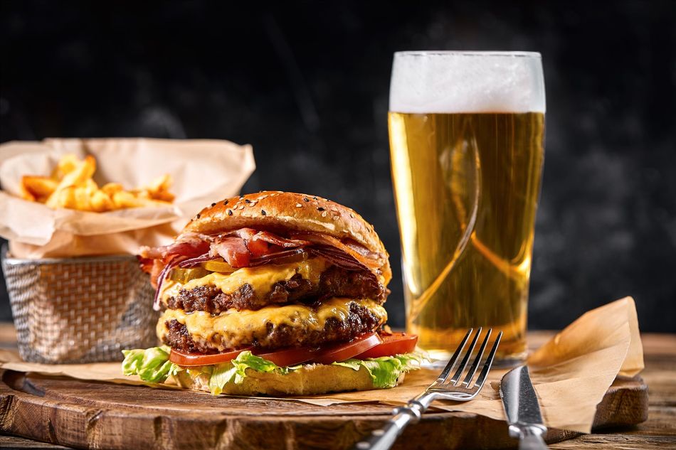 a hamburger and a glass of beer are on a wooden table .
