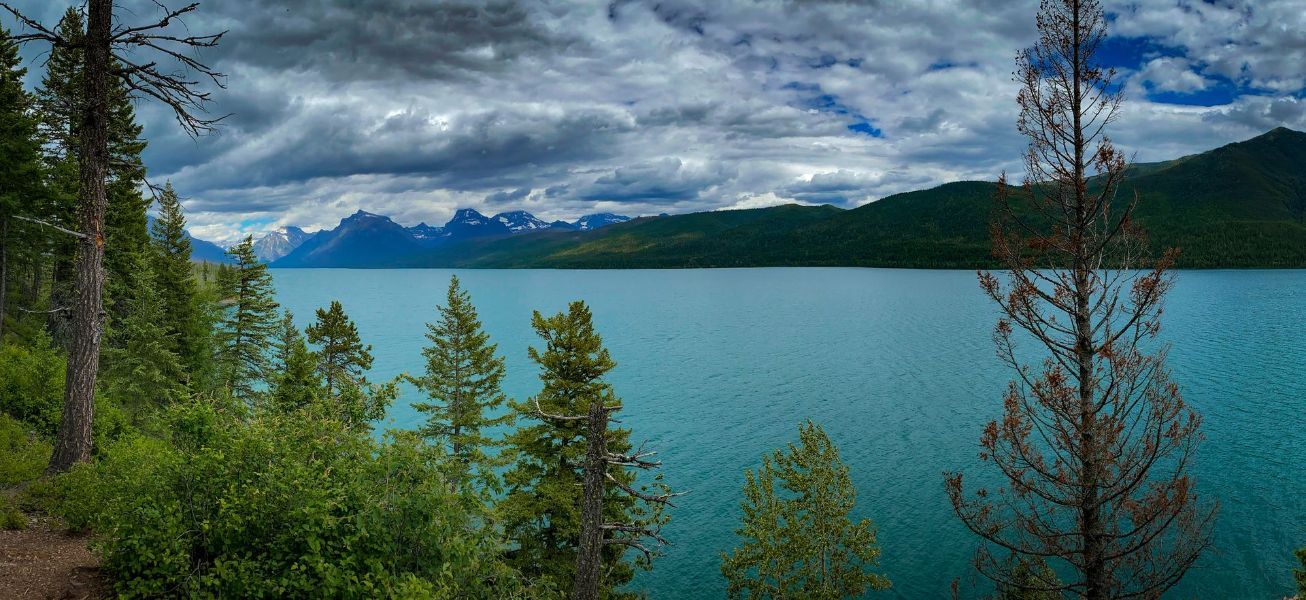 a lake surrounded by trees and mountains on a cloudy day .