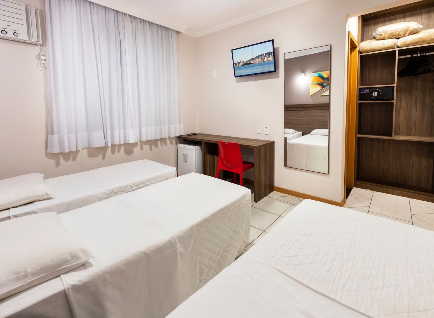 Um quarto de hotel com duas camas, uma escrivaninha, uma televisão e um espelho.