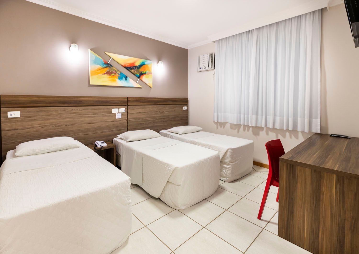 Um quarto de hotel com três camas e uma escrivaninha.