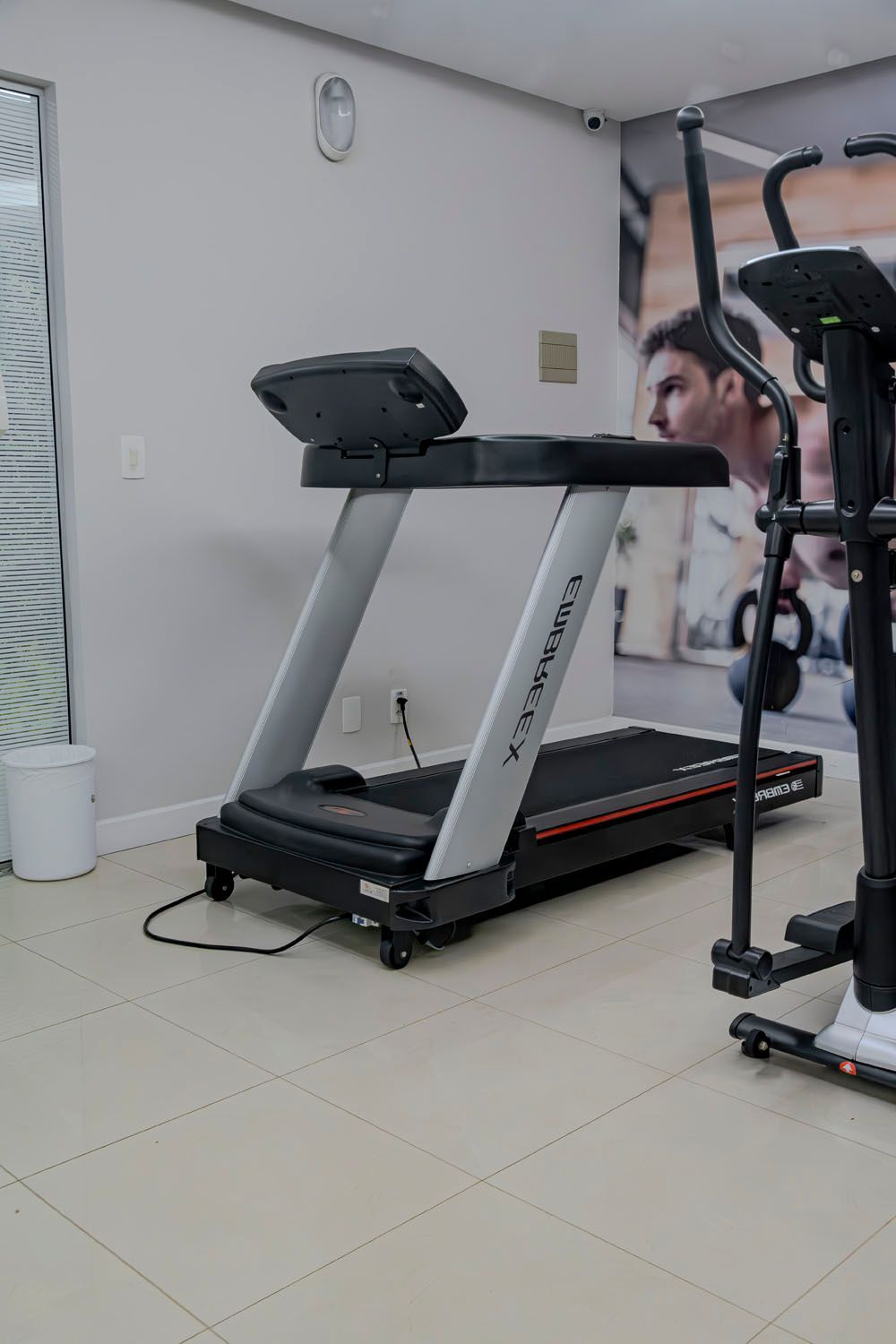 Uma esteira está em uma academia ao lado de uma máquina elíptica.