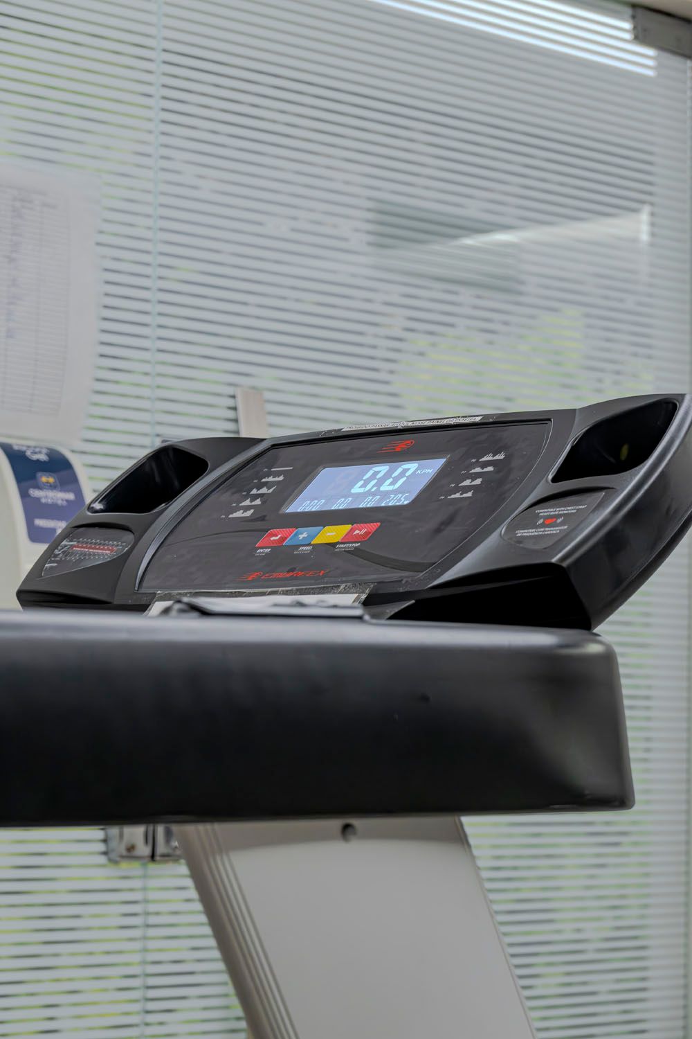 Uma esteira está em frente a uma janela em uma academia.