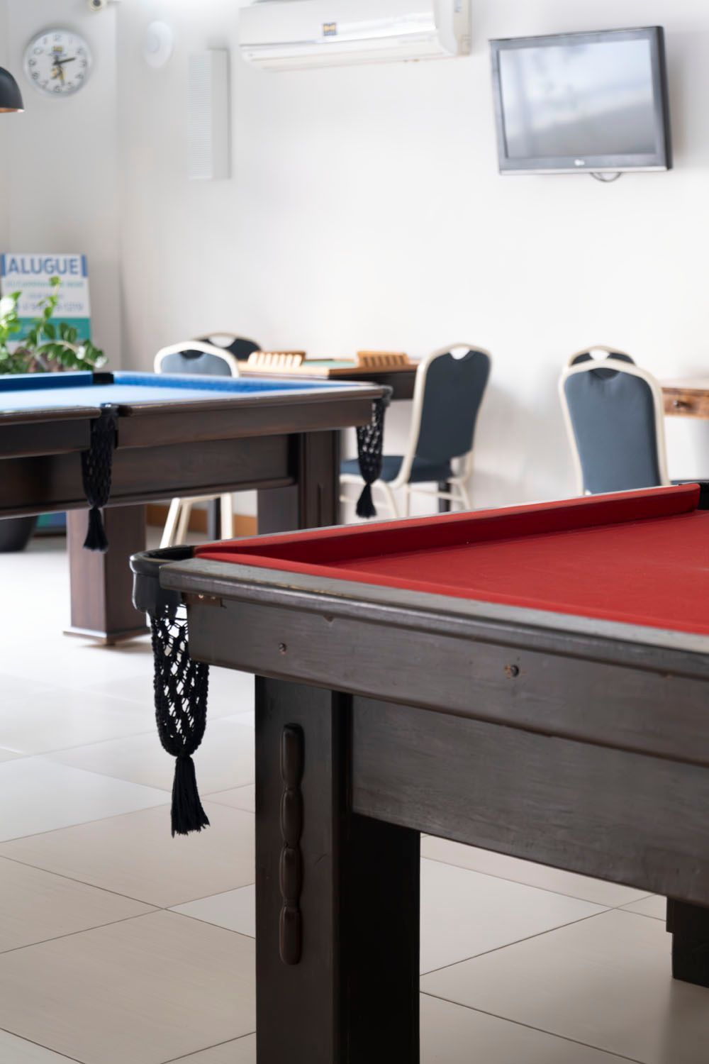 Uma mesa de sinuca com um pano vermelho está em uma sala com outras mesas de sinuca.