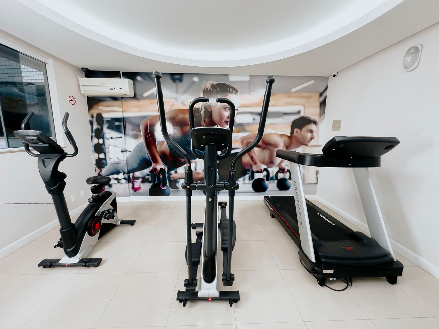 Uma academia com esteira, bicicleta ergométrica e aparelho elíptico.