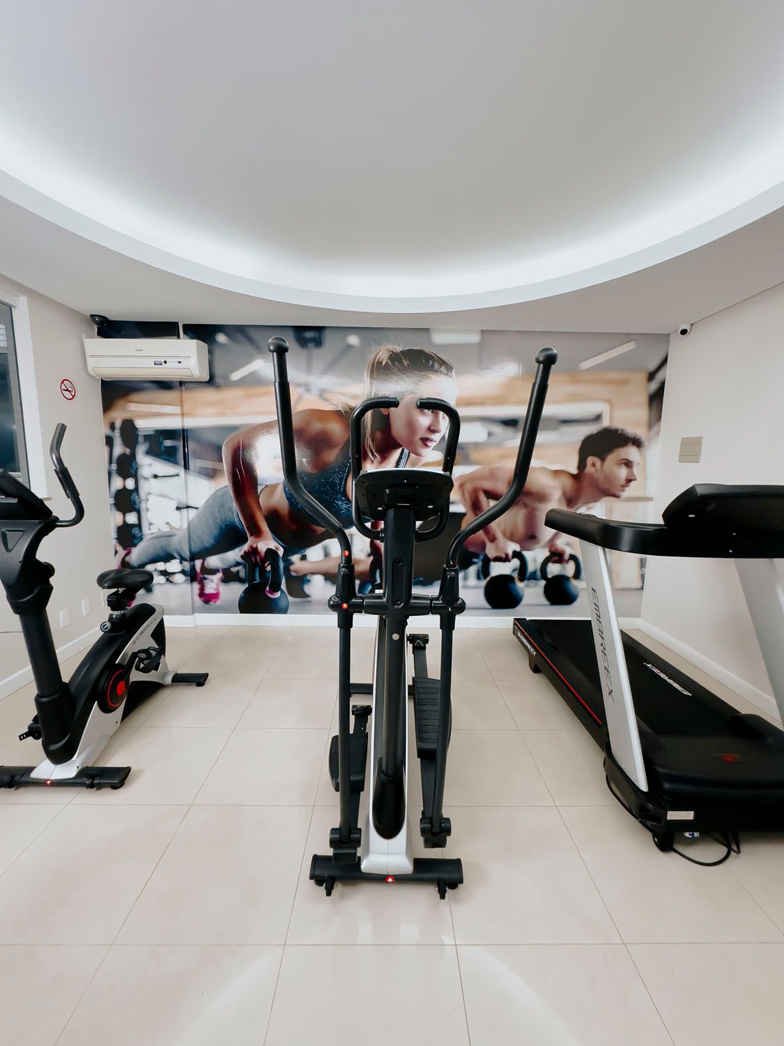 Uma academia com esteira, bicicleta ergométrica e aparelho elíptico.