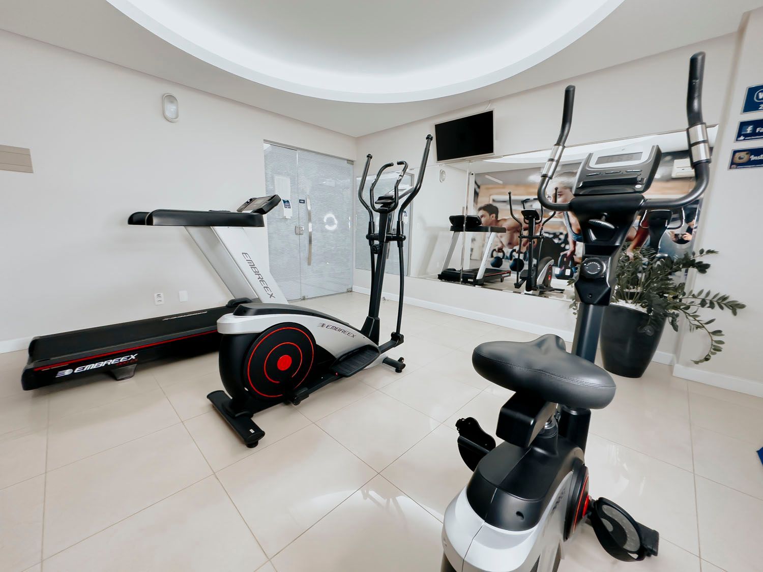 Uma academia com esteira, elíptico e bicicleta.