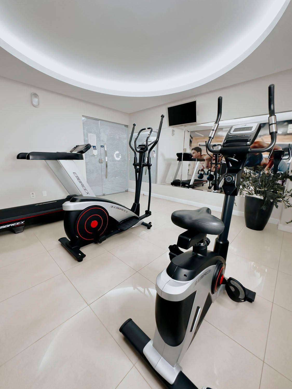 Uma academia com esteira, bicicleta ergométrica e aparelho elíptico.