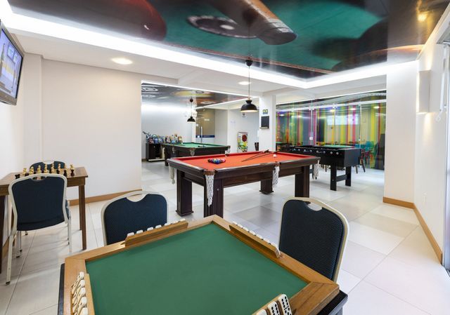 Uma sala de jogos com mesas de sinuca, mesas de xadrez e uma televisão.