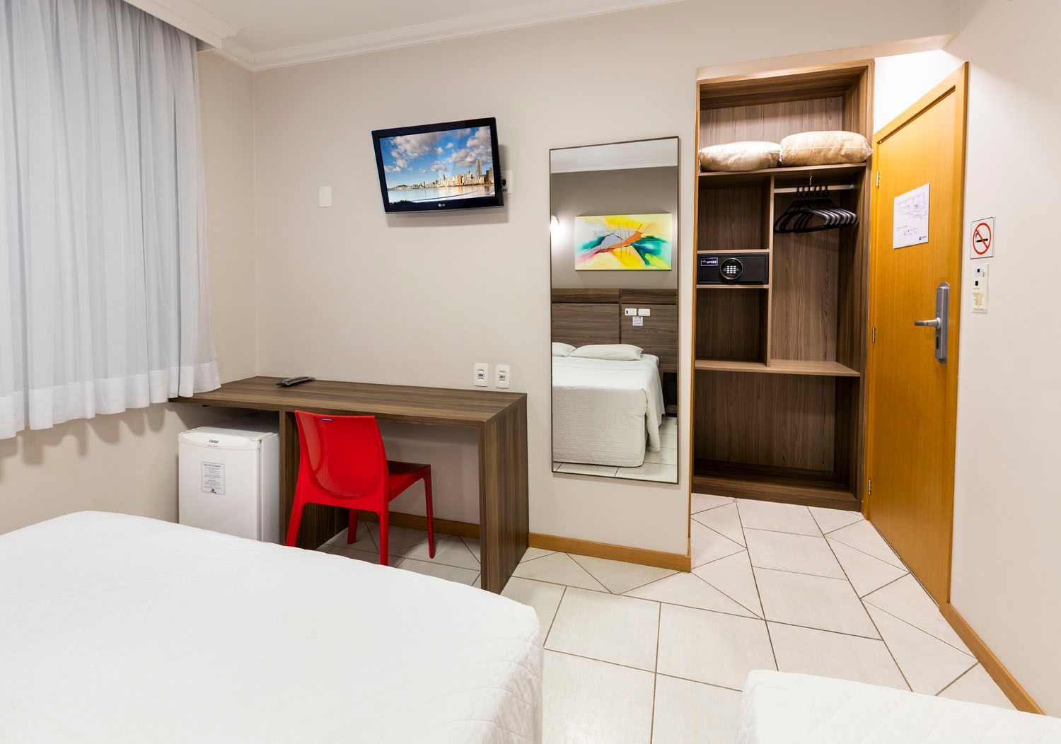 Um quarto de hotel com duas camas, uma escrivaninha, uma cadeira e uma televisão.