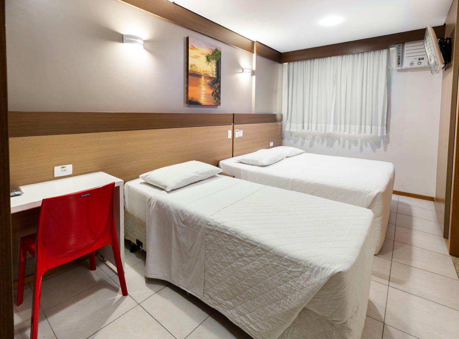 Um quarto de hotel com duas camas, uma escrivaninha e uma cadeira.