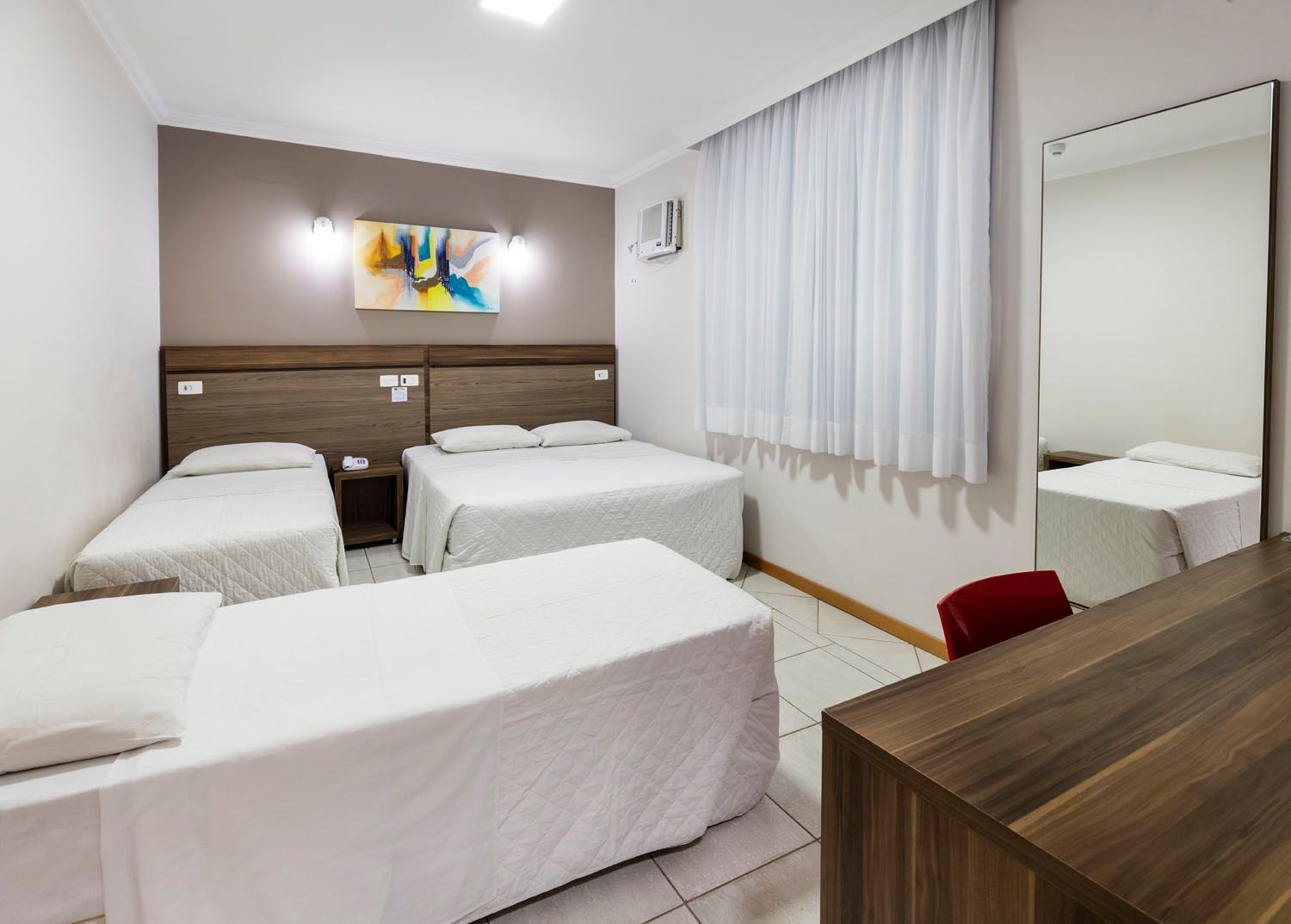 Um quarto de hotel com três camas e um espelho.