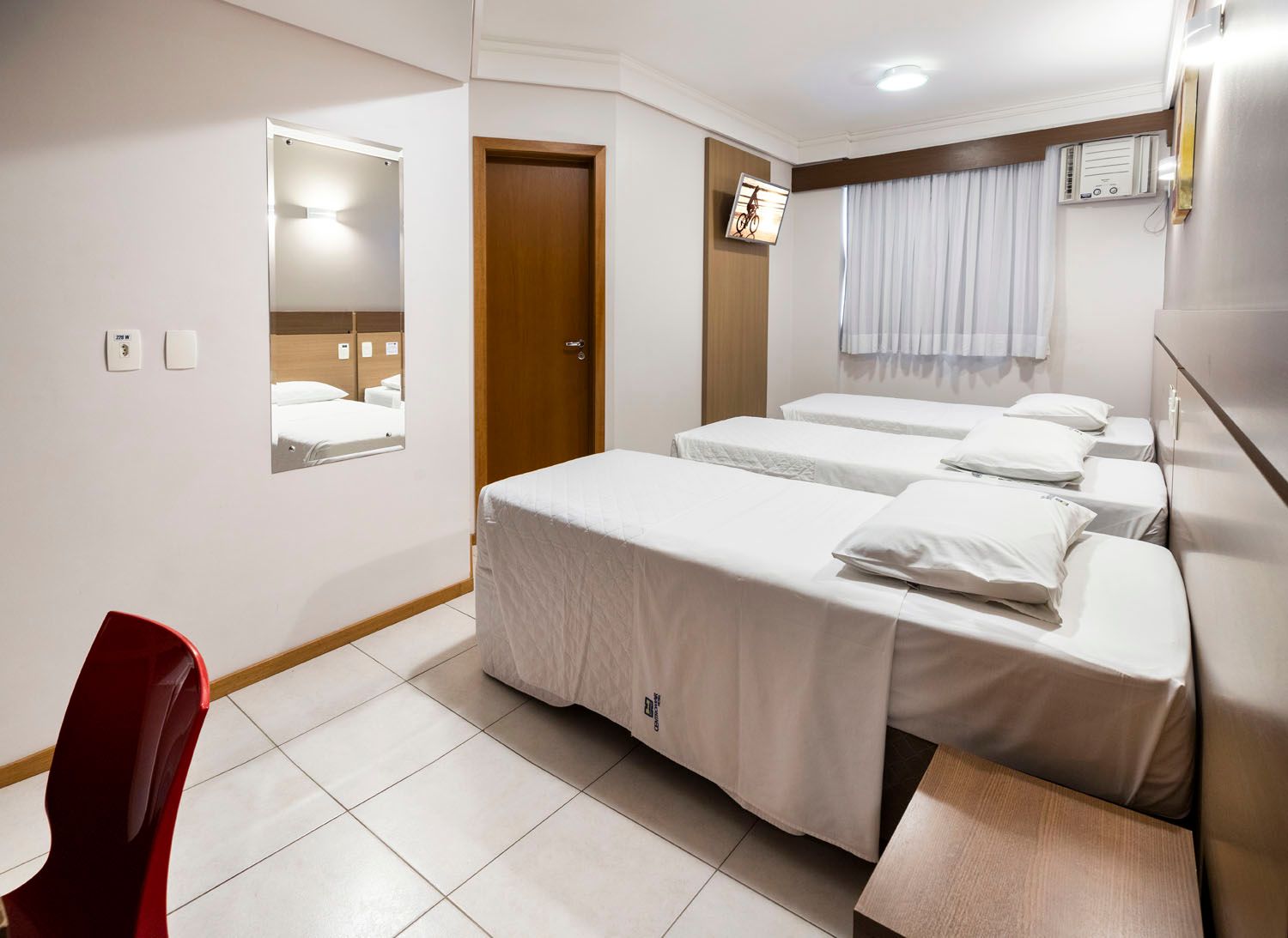 Um quarto de hotel com três camas e uma cadeira vermelha.