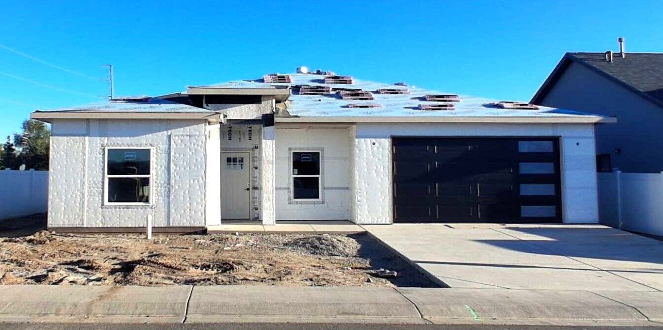 New construction home exterior in Grand Junction with white stucco and a black garage door.