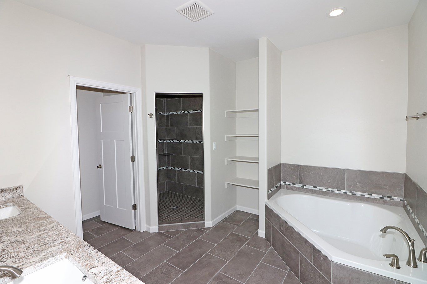 Gray tiled master bathroom with soaker tub and large shower.