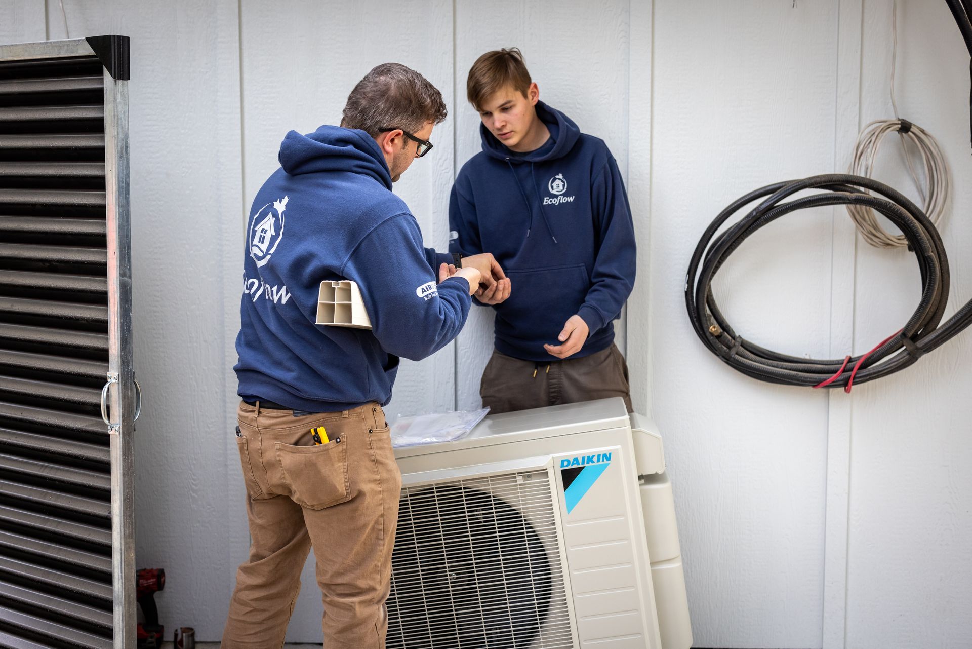 Two men are working on an air conditioner outside of a building.