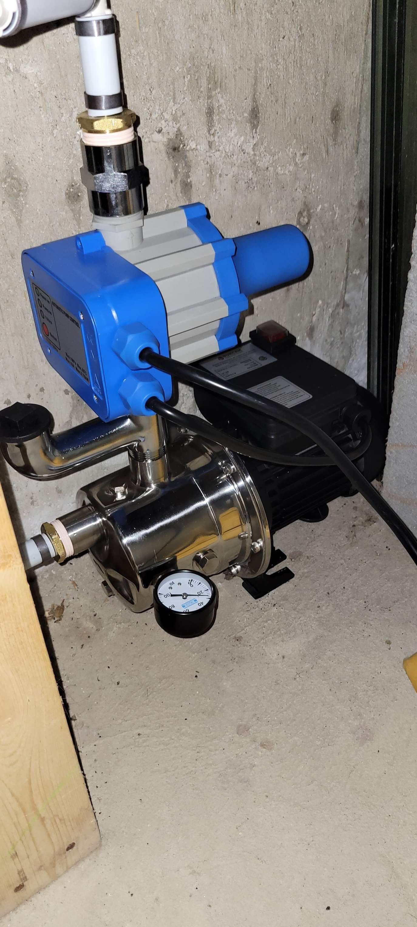 a blue water pump is sitting on the floor next to a pressure gauge .