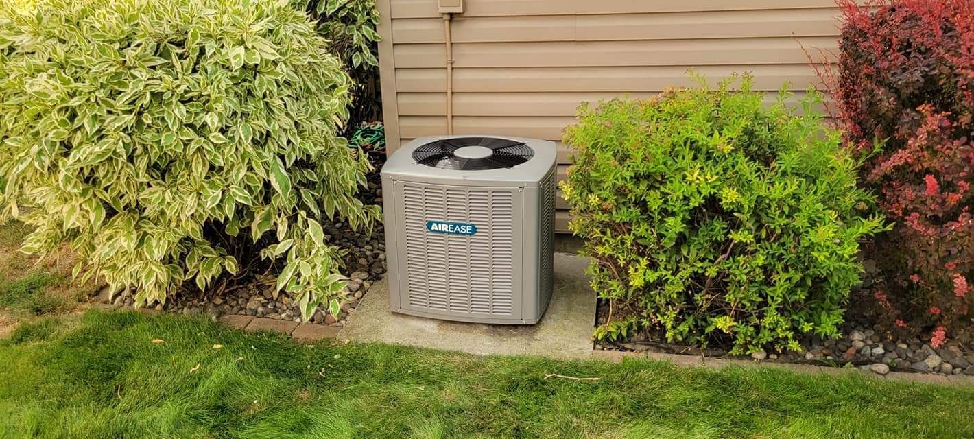 an air conditioner is sitting in the grass in front of a house .