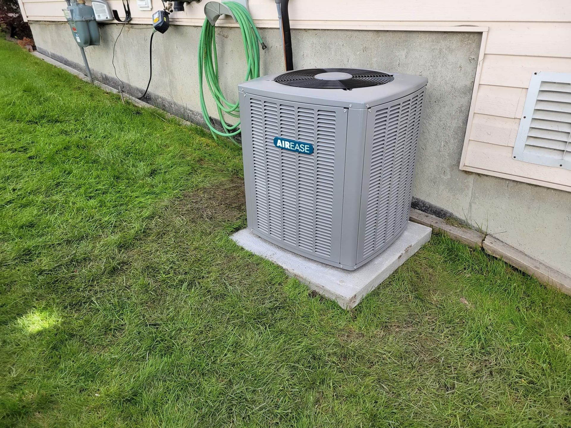 an air conditioner is sitting in the grass next to a house .