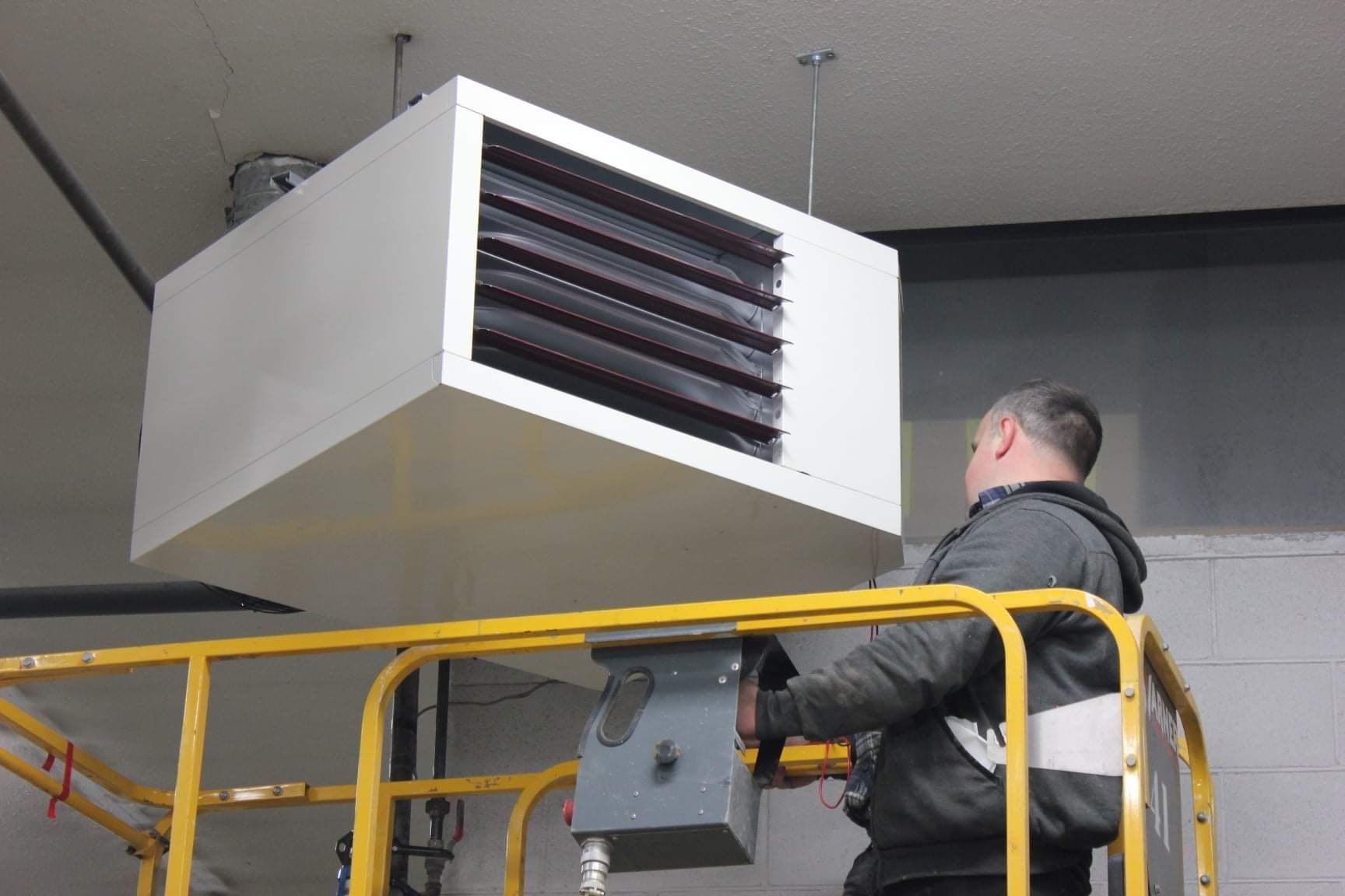 a man is working on a heater hanging from the ceiling .