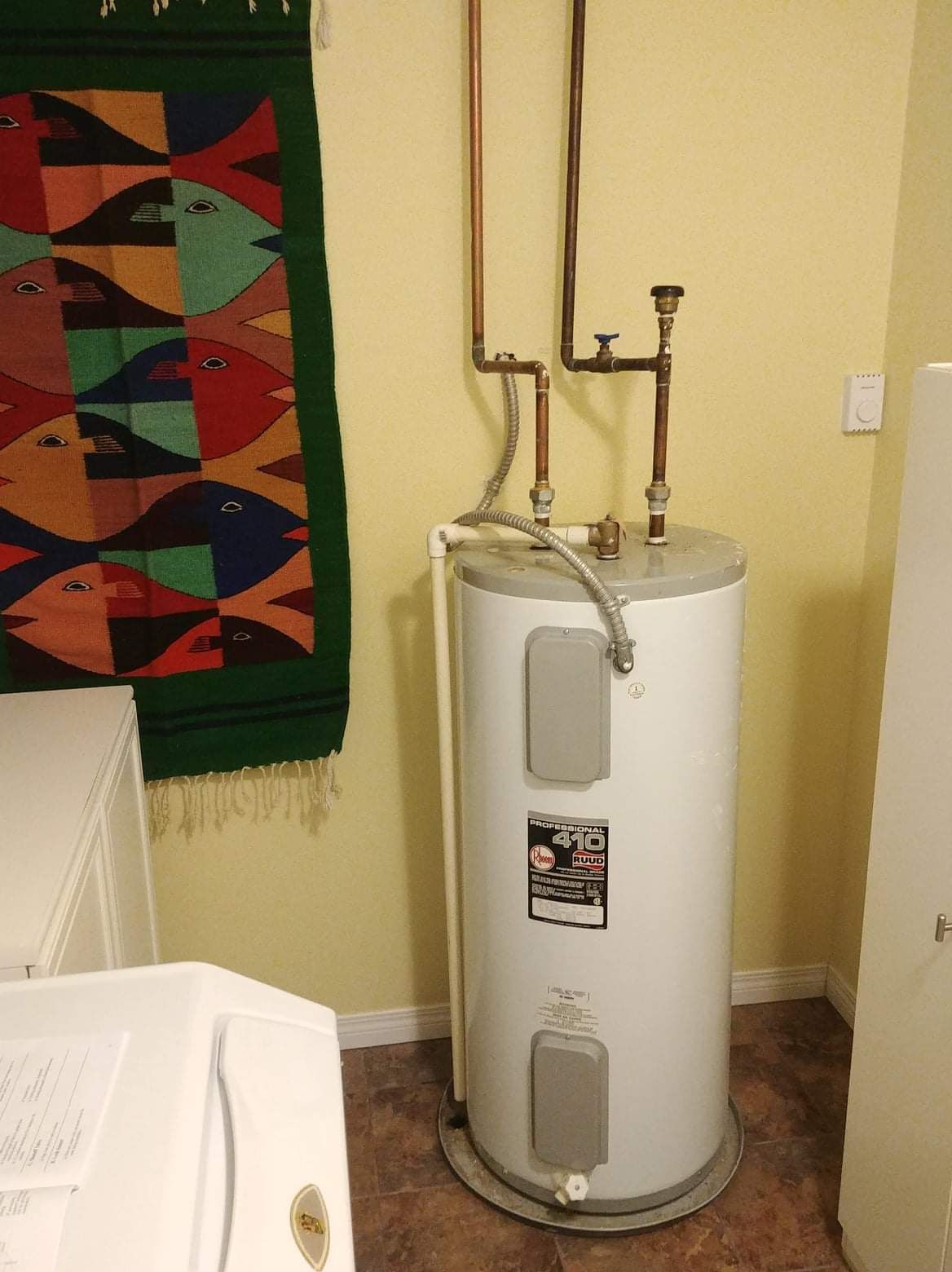 A water heater is sitting in a laundry room next to a washer and dryer