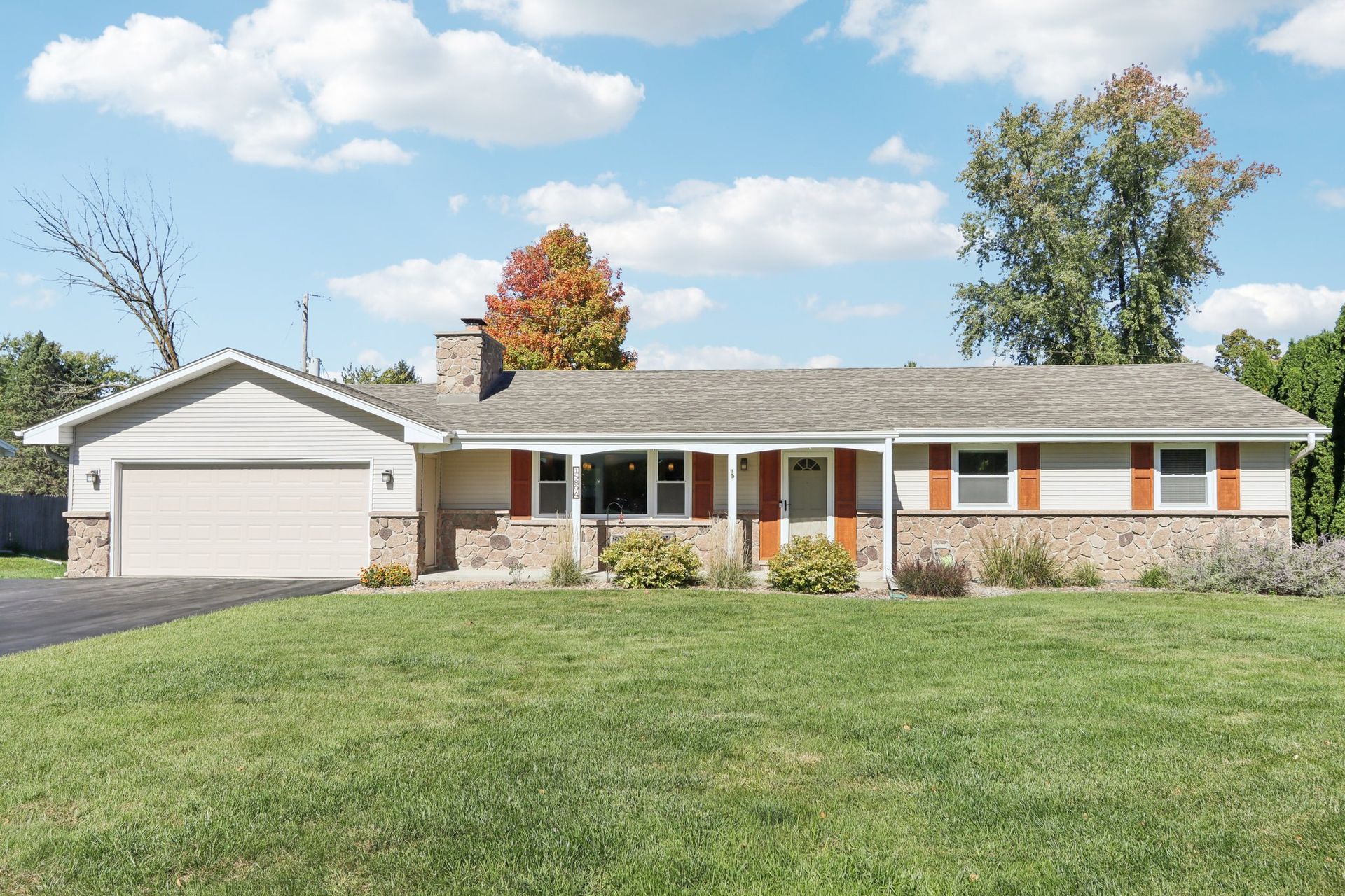 Single family Germantown, WI home with stone accents, orange shutters, garage, and green lawn under a blue sky.