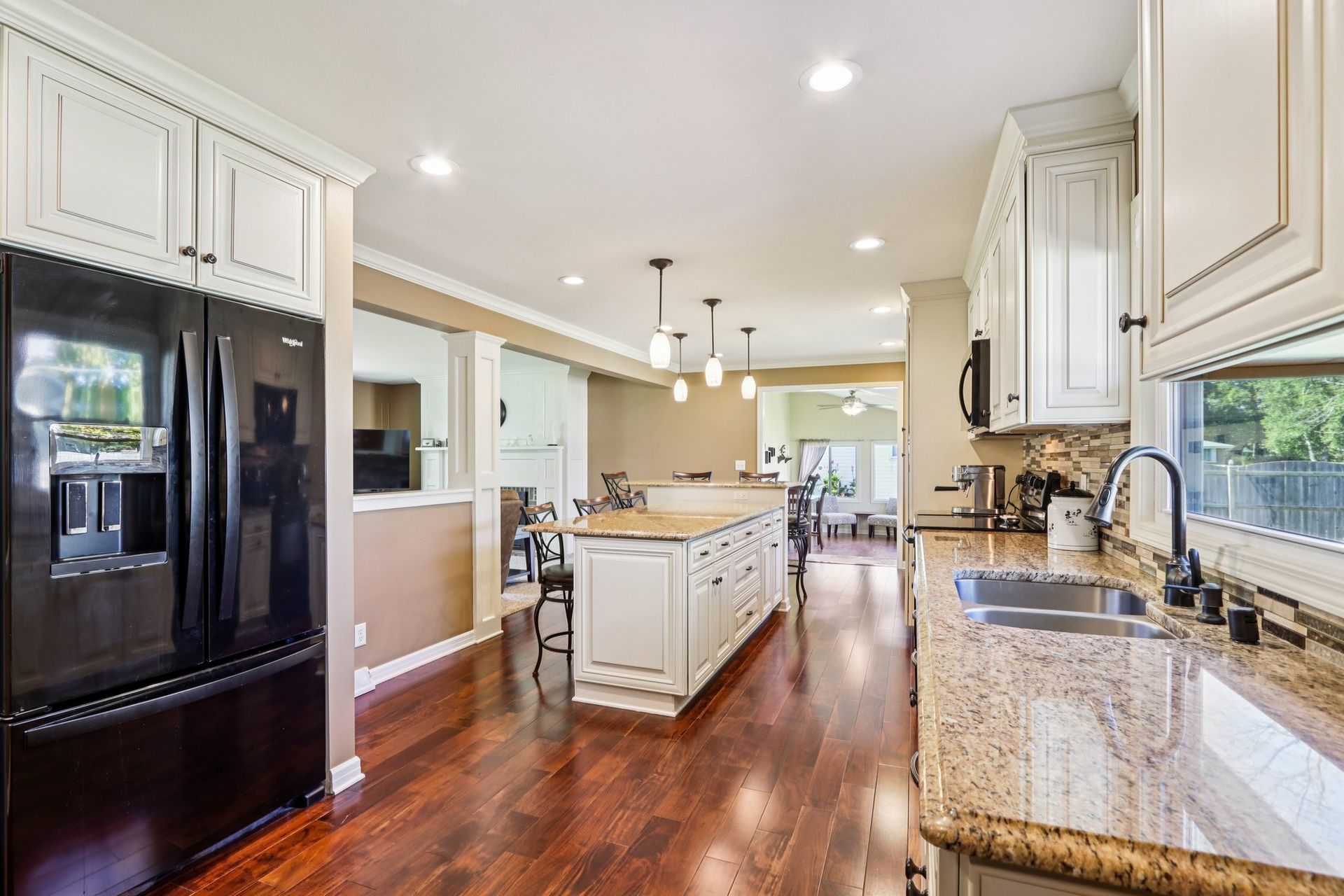 Kitchen with white cabinets, dark refrigerator, island, and wood floors.
