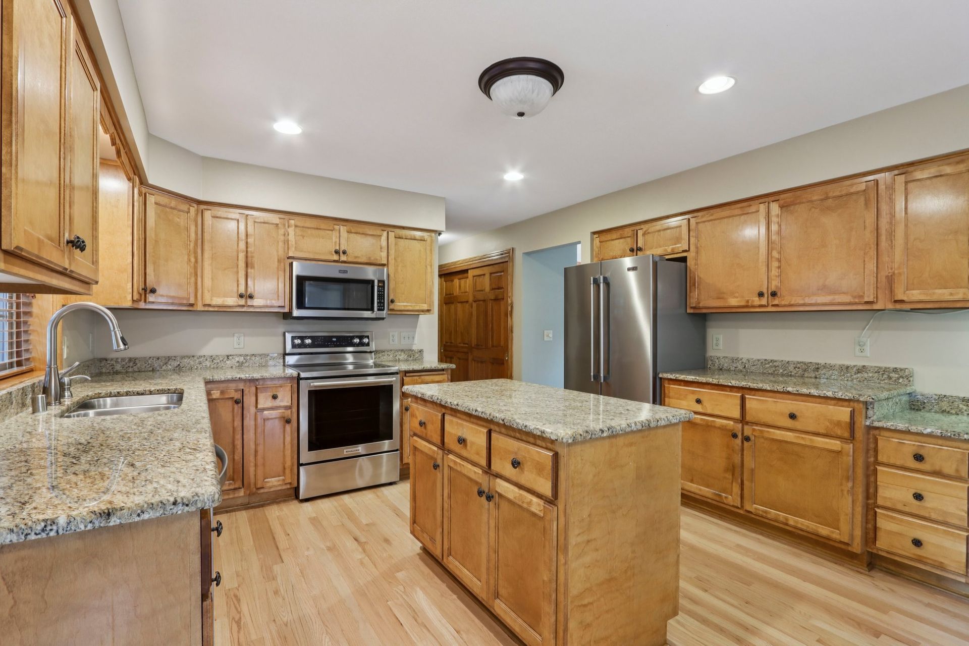 Kitchen with light wood cabinets, stainless steel appliances, granite countertops, and an island.
