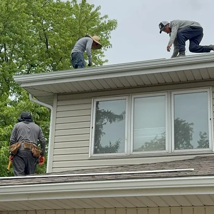 Three workers installing gutters on a house roof.