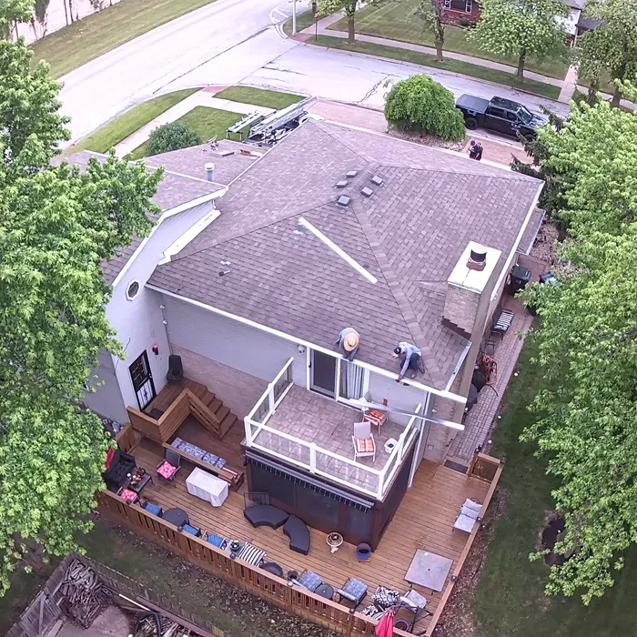 Overhead view of a house with a deck, trees, and workers on the roof.