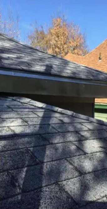 Two asphalt shingle roofs of different heights against a blue sky, one with visible gutters.