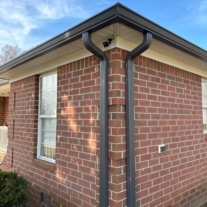 Dark gray gutters on a red brick house corner. A window is visible on the left. Bright sunny day.