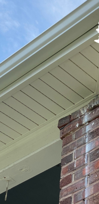 Brick exterior wall with white soffit and gutter against a blue sky.