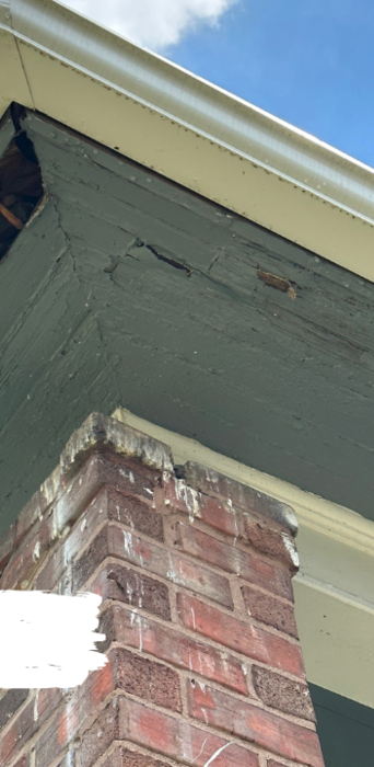 Brick pillar supporting a green painted overhang with a white gutter against a blue sky.