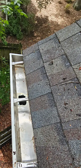 Close-up view of a roof with shingles and a gutter, trees in the background.