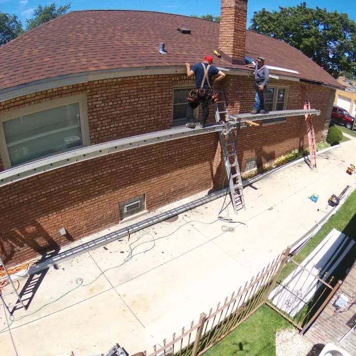 Tan vinyl-sided garage with white trim next to a narrow concrete path and a white structure.